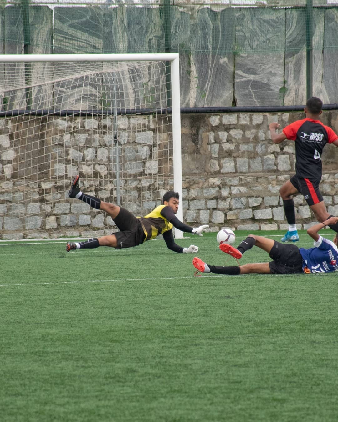 Young BPSS player celebrating a goal with arms raised and teammates rushing in to join